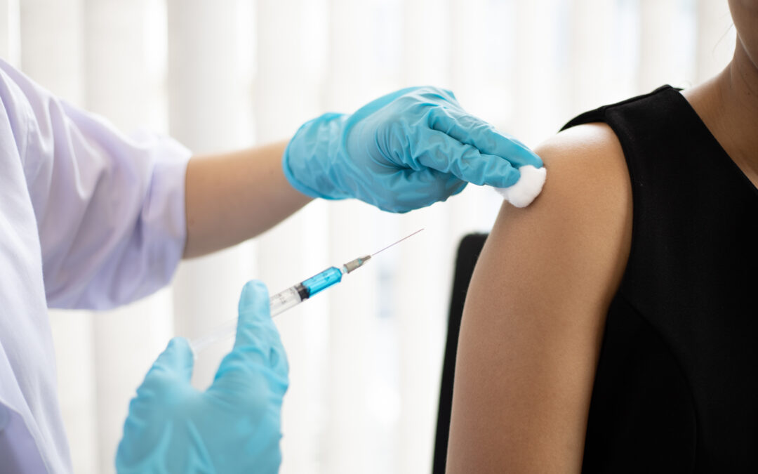Medical professional wearing blue gloves injecting a patient with a vaccine